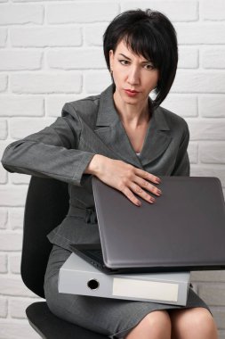 dizüstü bilgisayar ve stres, sahip klasörleri kızgın iş kadın giyinmiş önünde beyaz bir duvar, bir gri takım teşkil etmektedir