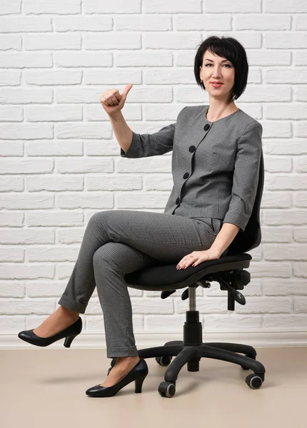 bir sandalyede oturan iş kadın giyinmiş önünde beyaz bir duvar, bir gri takım teşkil etmektedir