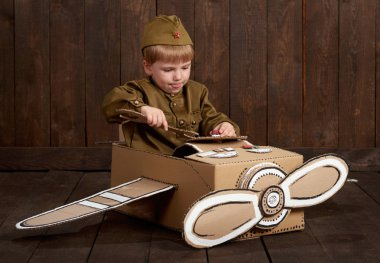 Çocuk Çocuk retro askeri üniformaları tamirde Polietilen, karton kutu, retro tarzı koyu ahşap arka plan bir uçak asker gibi giyinmiş