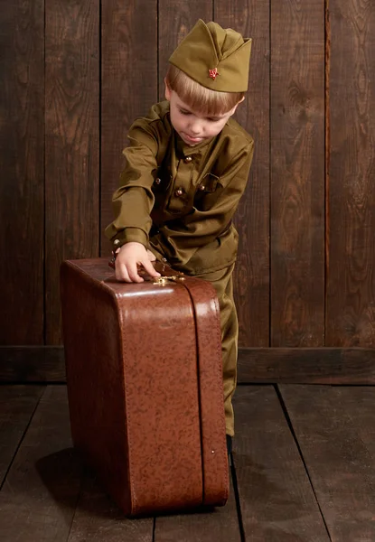 Çocuk Çocuk giymiş eski bavul, koyu ahşap arka plan, retro tarzı retro askeri üniformalı asker olarak