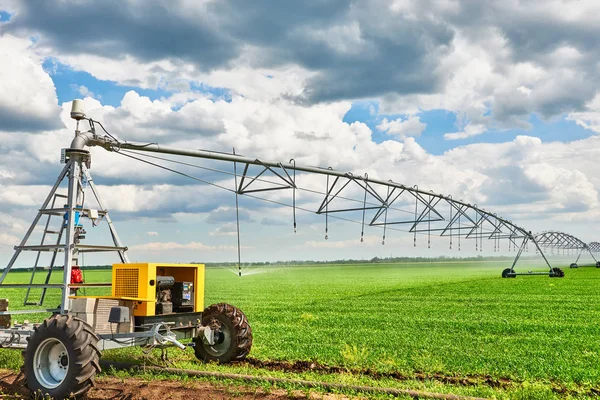 irrigation machine watering agricultural field with young sprouts, green plants on black soil and beautiful sky