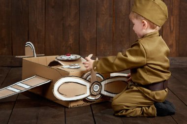 Çocuk Çocuk retro askeri üniformaları tamirde Polietilen, karton kutu, retro tarzı koyu ahşap arka plan bir uçak asker gibi giyinmiş