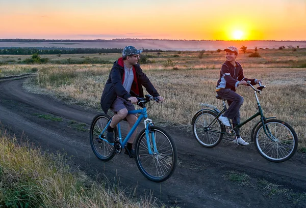 父と息子 夕方フィールド上国で自転車に乗る — ストック写真