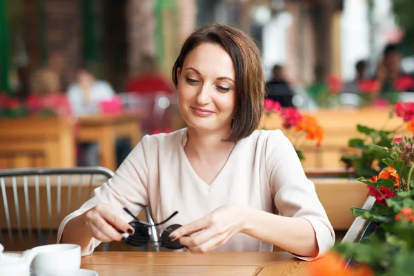 Young woman drinks coffee in cafeteria and posing with sunglasses