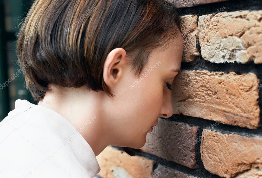 the young girl put her head to the brick wall, trouble concept