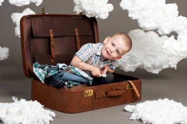 Çocuk bir bavulun içinde oturan ve bir yolculuk, bir dekorasyon, gri arka plan olarak Pamuk yün sıkıntısı devam