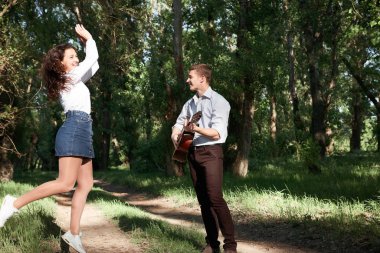 Genç çift, ormanda yürüyüş gitar çalmak ve dans, yaz doğa, parlak güneş ışığı, gölgeler ve yeşil yaprakları, romantik duygular