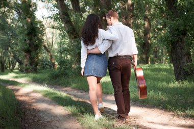 Genç çift, ormanda yürüyüş gitar çalmak ve dans, yaz doğa, parlak güneş ışığı, gölgeler ve yeşil yaprakları, romantik duygular