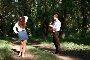 Genç çift, ormanda yürüyüş gitar çalmak ve dans, yaz doğa, parlak güneş ışığı, gölgeler ve yeşil yaprakları, romantik duygular