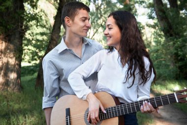 Genç çift, ormanda yürüyüş gitar çalmak ve dans, yaz doğa, parlak güneş ışığı, gölgeler ve yeşil yaprakları, romantik duygular