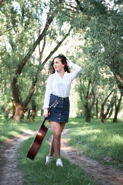 ormanda yürüyüş ve iskambil gitar, yaz doğa, parlak güneş ışığı, gölgeler ve yeşil yaprakları, romantik duygular genç kadın