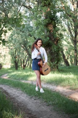 ormanda yürüyüş ve iskambil gitar, yaz doğa, parlak güneş ışığı, gölgeler ve yeşil yaprakları, romantik duygular genç kadın