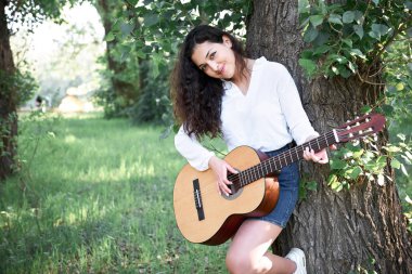 ormanda yürüyüş ve iskambil gitar, yaz doğa, parlak güneş ışığı, gölgeler ve yeşil yaprakları, romantik duygular genç kadın