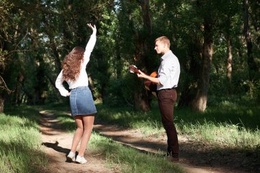 Genç çift, ormanda yürüyüş gitar çalmak ve dans, yaz doğa, parlak güneş ışığı, gölgeler ve yeşil yaprakları, romantik duygular