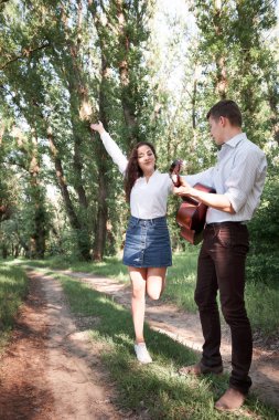 Genç çift, ormanda yürüyüş gitar çalmak ve dans, yaz doğa, parlak güneş ışığı, gölgeler ve yeşil yaprakları, romantik duygular