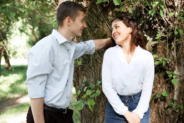 若いカップルが森の中を歩いて 近くの木 夏の自然 明るい日光の下ポーズ影と緑の葉 恋愛感情 — ストック写真