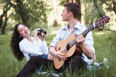 ormanda oturan ve fotoğrafta eski fotoğraf makinesi, yaz doğa, parlak güneş ışığı, gitar, çalmak genç çift gölgeler ve yeşil yaprakları, romantik duygular