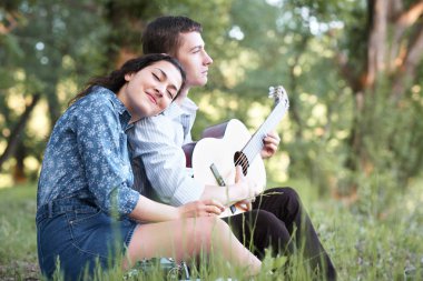 Genç çift ormanda oturan ve iskambil gitar, yaz doğa, parlak güneş ışığı, gölgeler ve yeşil yaprakları, romantik duygular