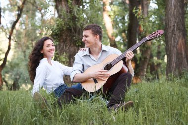 Genç çift ormanda oturan ve iskambil gitar, yaz doğa, parlak güneş ışığı, gölgeler ve yeşil yaprakları, romantik duygular