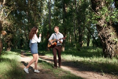 Genç çift, ormanda yürüyüş gitar çalmak ve dans, yaz doğa, parlak güneş ışığı, gölgeler ve yeşil yaprakları, romantik duygular