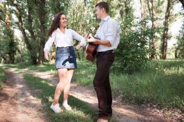Genç çift, ormanda yürüyüş gitar çalmak ve dans, yaz doğa, parlak güneş ışığı, gölgeler ve yeşil yaprakları, romantik duygular
