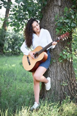 ormanda yürüyüş ve iskambil gitar, yaz doğa, parlak güneş ışığı, gölgeler ve yeşil yaprakları, romantik duygular genç kadın