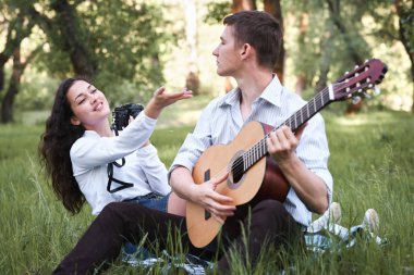 ormanda oturan ve fotoğrafta eski fotoğraf makinesi, yaz doğa, parlak güneş ışığı, gitar, çalmak genç çift gölgeler ve yeşil yaprakları, romantik duygular