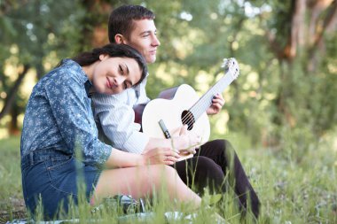 Genç çift ormanda oturan ve iskambil gitar, yaz doğa, parlak güneş ışığı, gölgeler ve yeşil yaprakları, romantik duygular