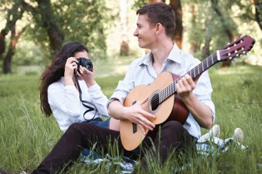 ormanda oturan ve fotoğrafta eski fotoğraf makinesi, yaz doğa, parlak güneş ışığı, gitar, çalmak genç çift gölgeler ve yeşil yaprakları, romantik duygular