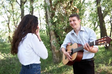 Genç çift, ormanda yürüyüş gitar çalmak ve dans, yaz doğa, parlak güneş ışığı, gölgeler ve yeşil yaprakları, romantik duygular