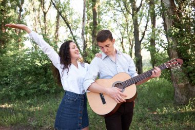 Genç çift, ormanda yürüyüş gitar çalmak ve dans, yaz doğa, parlak güneş ışığı, gölgeler ve yeşil yaprakları, romantik duygular