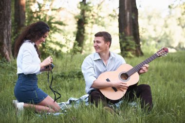 ormanda oturan ve fotoğrafta eski fotoğraf makinesi, yaz doğa, parlak güneş ışığı, gitar, çalmak genç çift gölgeler ve yeşil yaprakları, romantik duygular