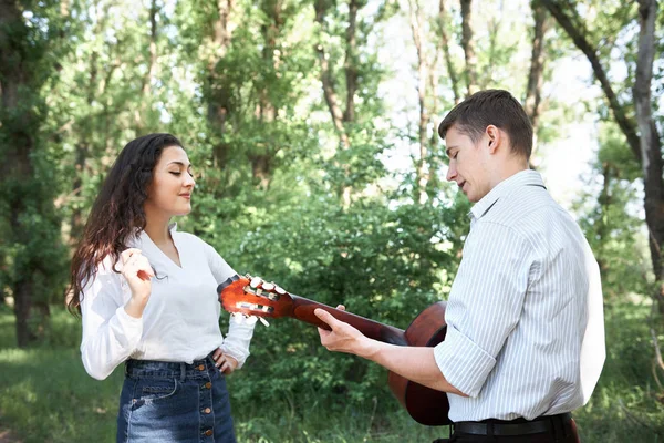 Genç çift, ormanda yürüyüş gitar çalmak ve dans, yaz doğa, parlak güneş ışığı, gölgeler ve yeşil yaprakları, romantik duygular