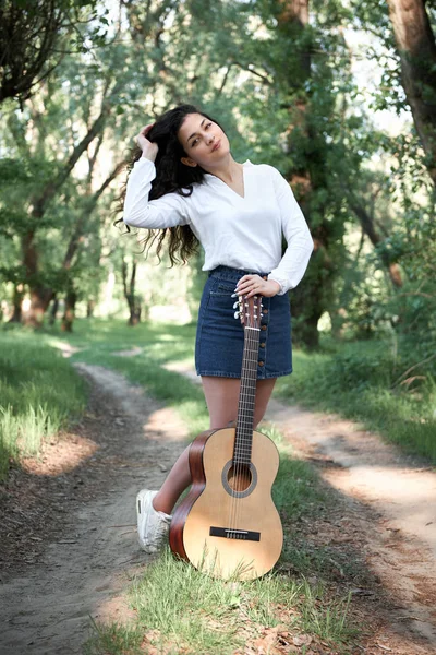 ormanda yürüyüş ve iskambil gitar, yaz doğa, parlak güneş ışığı, gölgeler ve yeşil yaprakları, romantik duygular genç kadın