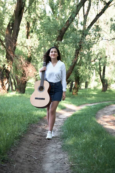 ormanda yürüyüş ve iskambil gitar, yaz doğa, parlak güneş ışığı, gölgeler ve yeşil yaprakları, romantik duygular genç kadın