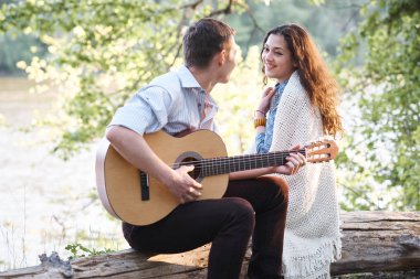 Genç çift, bir günlük nehrin yanında oturan ve iskambil gitar, yaz doğa, parlak güneş ışığı gölgeler ve yeşil yaprakları, romantik duygular