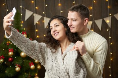 Mutlu çift selfie alarak ve Noel dekorasyonu eğleniyor. Koyu ahşap iç ışıkları ile. Romantik akşam ve sevgi kavramı. Yeni yıl tatili.
