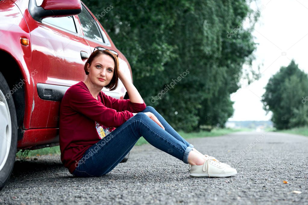young girl sitting on the road by the red car