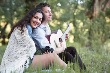 Genç çift ormanda oturan ve iskambil gitar, yaz doğa, parlak güneş ışığı, gölgeler ve yeşil yaprakları, romantik duygular