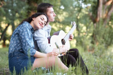 Genç çift ormanda oturan ve iskambil gitar, yaz doğa, parlak güneş ışığı, gölgeler ve yeşil yaprakları, romantik duygular