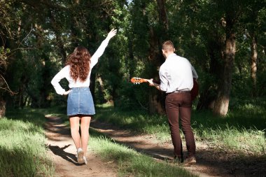 Genç çift, ormanda yürüyüş gitar çalmak ve dans, yaz doğa, parlak güneş ışığı, gölgeler ve yeşil yaprakları, romantik duygular