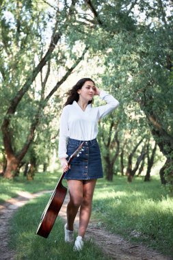 ormanda yürüyüş ve iskambil gitar, yaz doğa, parlak güneş ışığı, gölgeler ve yeşil yaprakları, romantik duygular genç kadın