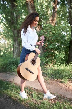 ormanda yürüyüş ve iskambil gitar, yaz doğa, parlak güneş ışığı, gölgeler ve yeşil yaprakları, romantik duygular genç kadın