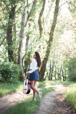 ormanda yürüyüş ve iskambil gitar, yaz doğa, parlak güneş ışığı, gölgeler ve yeşil yaprakları, romantik duygular genç kadın