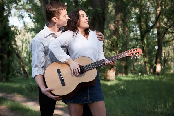 Genç çift, ormanda yürüyüş gitar çalmak ve dans, yaz doğa, parlak güneş ışığı, gölgeler ve yeşil yaprakları, romantik duygular