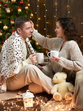 Çay içme ve Noel dekorasyonu, koyu ahşap iç ışıkları ile katta oturan konuşan mutlu çift. Romantik akşam ve sevgi kavramı. Yeni yıl tatili.