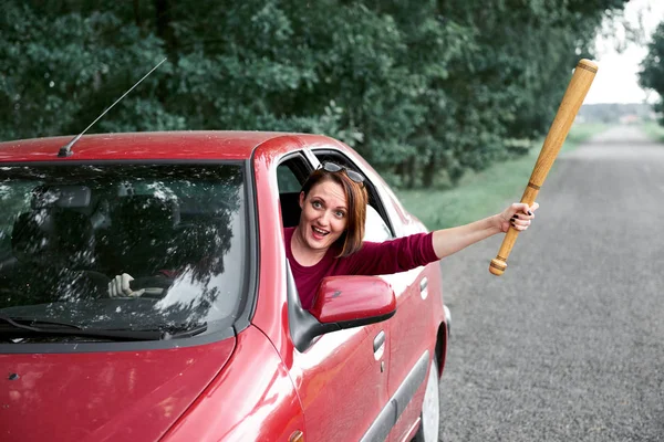 young female driver has stress and anger, threatens with a baseball bat, has a red car