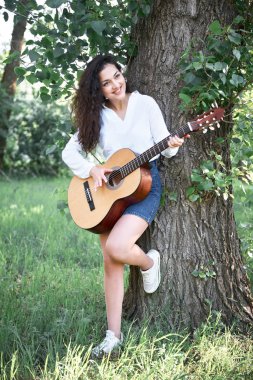 ormanda yürüyüş ve iskambil gitar, yaz doğa, parlak güneş ışığı, gölgeler ve yeşil yaprakları, romantik duygular genç kadın