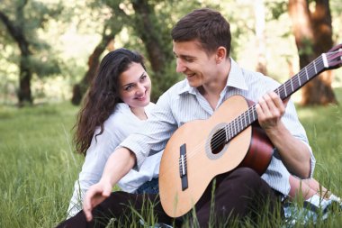 Genç çift ormanda oturan ve iskambil gitar, yaz doğa, parlak güneş ışığı, gölgeler ve yeşil yaprakları, romantik duygular