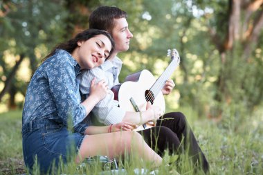 Genç çift ormanda oturan ve iskambil gitar, yaz doğa, parlak güneş ışığı, gölgeler ve yeşil yaprakları, romantik duygular
